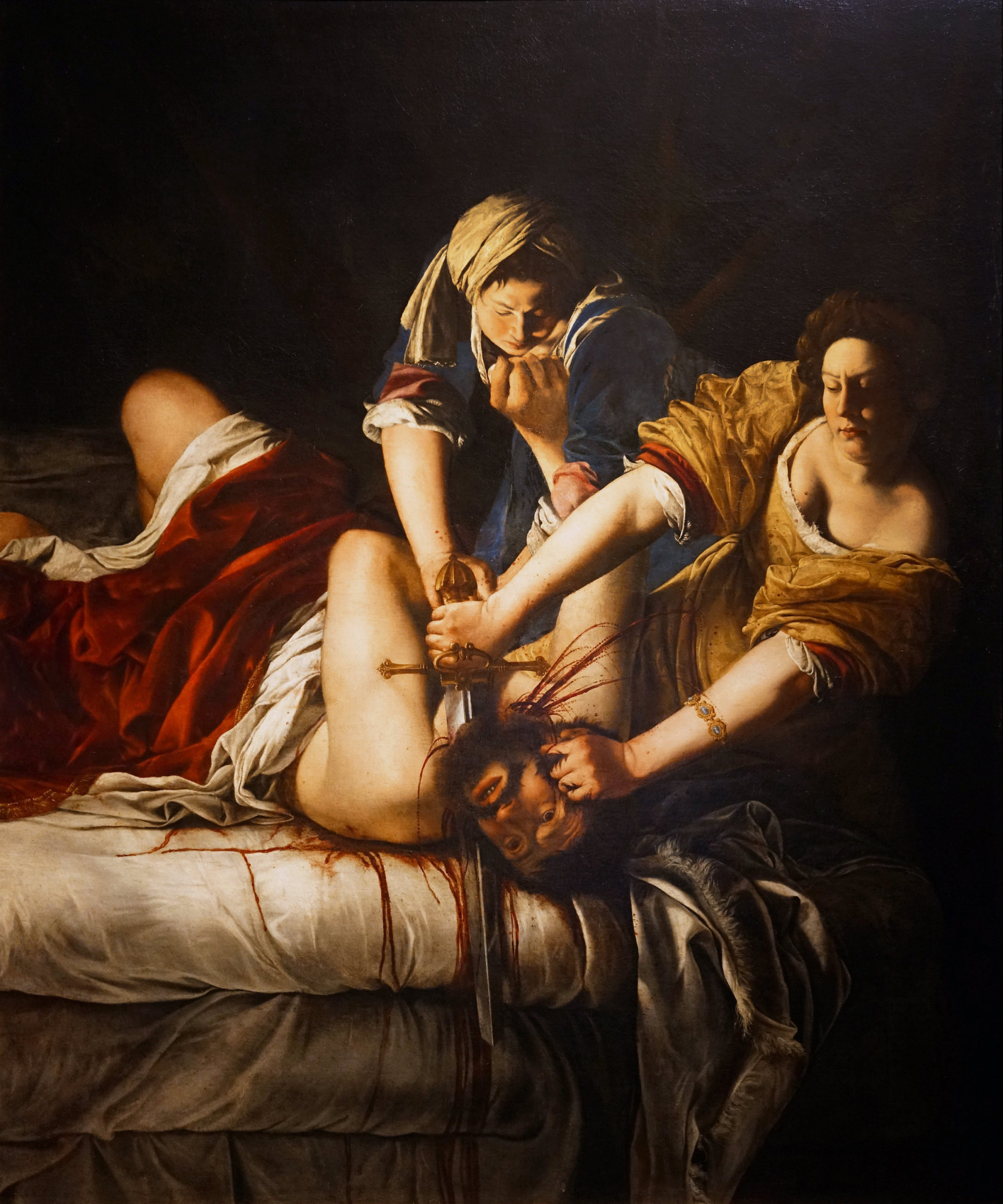 Artemisia Gentileschi's Judith Slaying Holofernes shows Judith and her maidservant in the middle of decapitating Holofernes. The painting has deep rich colors and a strong contrast of light and shadow.
