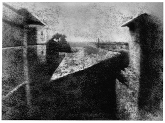 A black and white photograph depicting a high-contrast, grainy view of a narrow pathway or bridge between two buildings with a distant horizon. The composition emphasizes strong shadows and geometric shapes, creating a moody, abstract atmosphere.