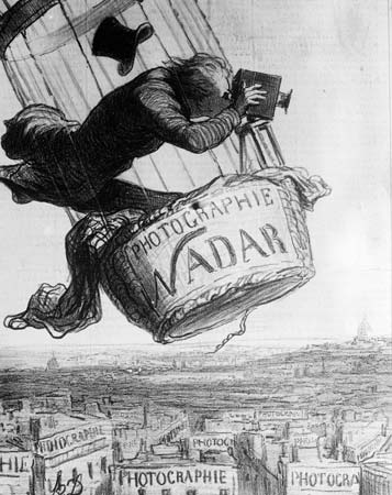 A black and white illustration depicts a man operating an early camera mounted on a hot air balloon basket labeled "Photographie Nadar." The scene shows multiple rooftops below with signs reading "Photographie," emphasizing the rise of photography and aerial perspectives in the 19th century.