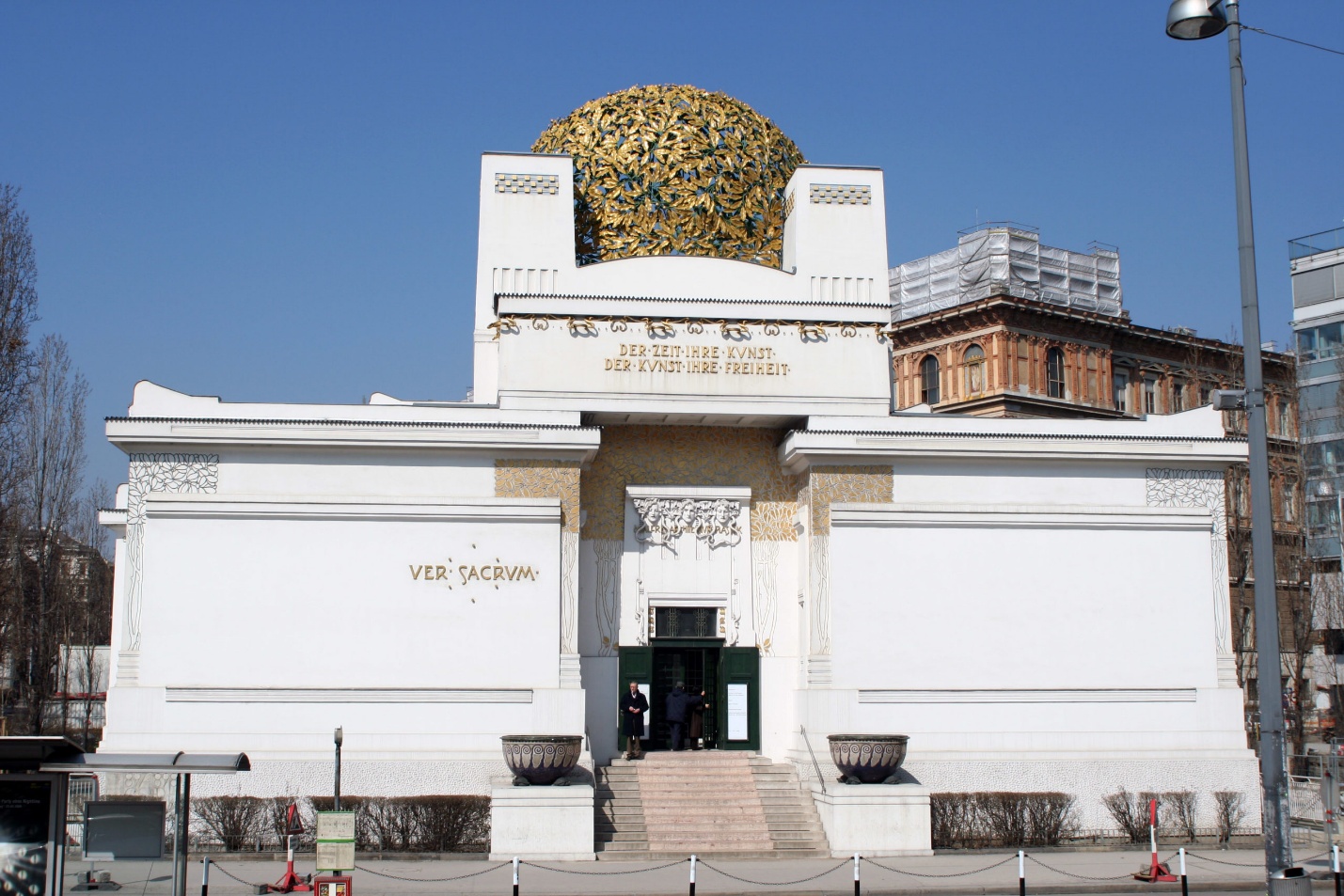 Photograph of Secession Building in Vienna, an example of Art Nouveau architecture featuring a white facade with gold accents and a distinctive golden dome made of laurel leaves. The building serves as an exhibition hall for contemporary art, with visible inscriptions and ornamental details highlighting its cultural significance.