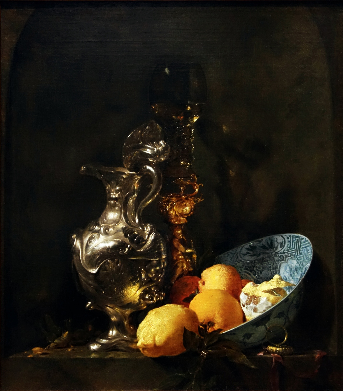 Still life painting featuring a silver pitcher, ornate golden goblet, and a blue patterned bowl filled with lemons and a peeled lemon segment. Dark background contrasts with reflective metal surfaces and vibrant yellow fruit, emphasizing texture and light.