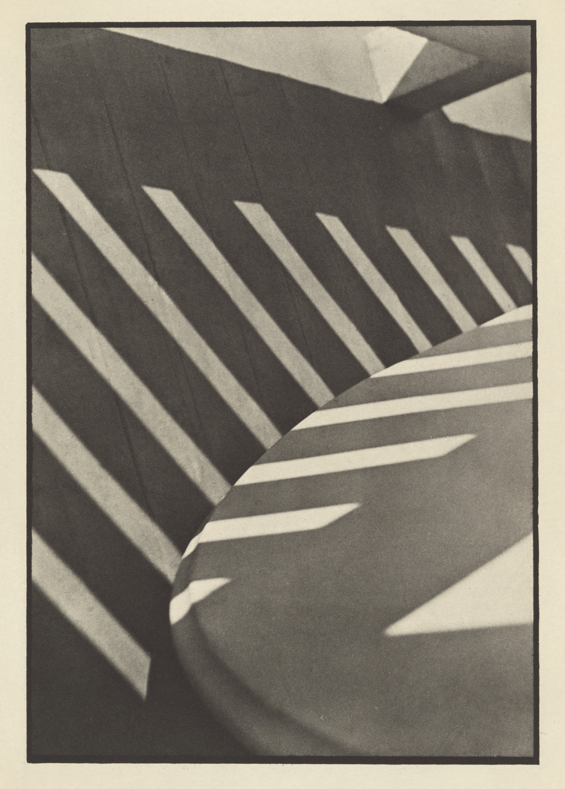 Black and white photograph showing diagonal shadows cast by a railing onto a curved surface, creating a pattern of alternating light and dark stripes. The composition emphasizes geometric shapes and contrast between light and shadow.