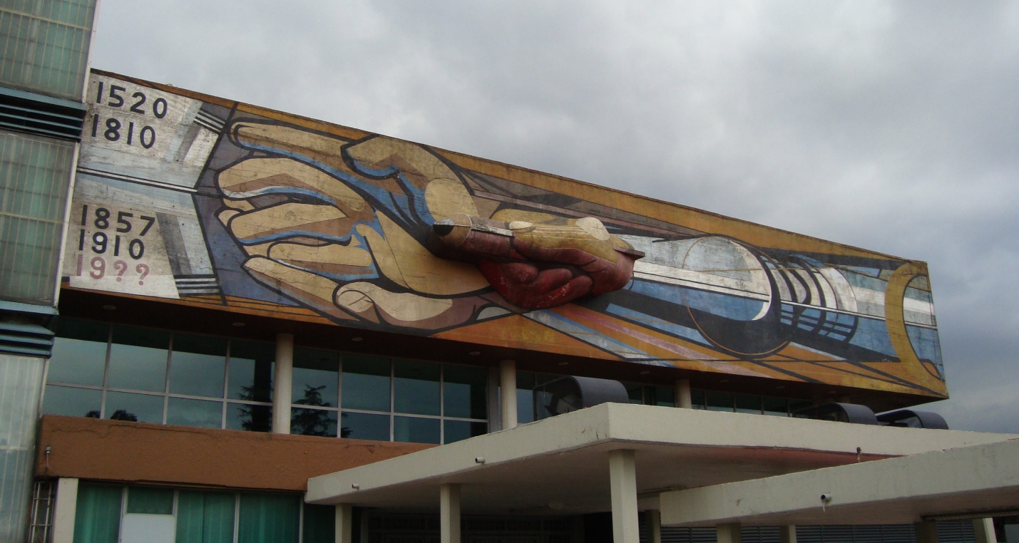 Photograph of a large mural on a building facade depicting two hands reaching toward each other, with a heart in the center and a ship on the right side. The mural includes years 1520, 1810, 1857, 1910, and a partially obscured date, suggesting historical or cultural significance.