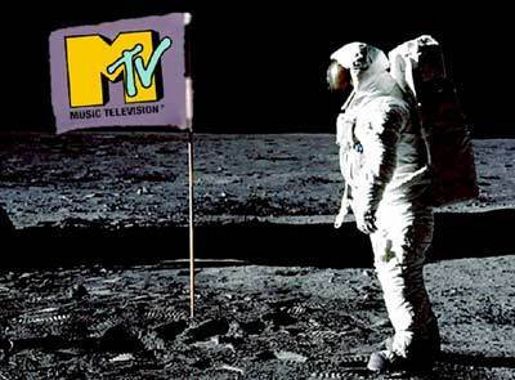 Photograph of an astronaut standing on a lunar surface next to a flag featuring the MTV logo in yellow and green on a purple background. The scene combines iconic moon landing imagery with MTV branding.