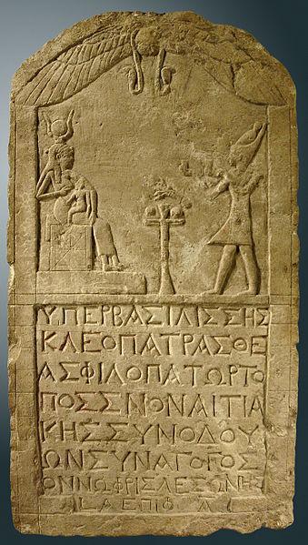 Stone tablet with carving depicting Cleopatra venerating the goddess Isis, with an inscription in Greek at the bottom.
